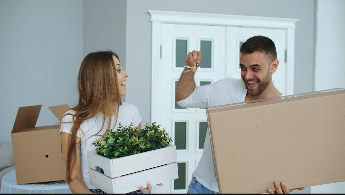 A couple laughing at the front door of their new house, holding up the keys