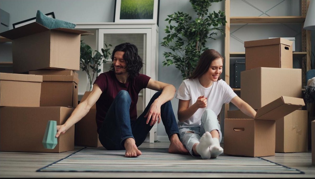 A couple sitting on the floor of their new living room, unpacking boxes